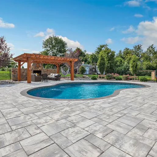 Freeform pool with stone paver patio, wood pergola, and outdoor fireplace