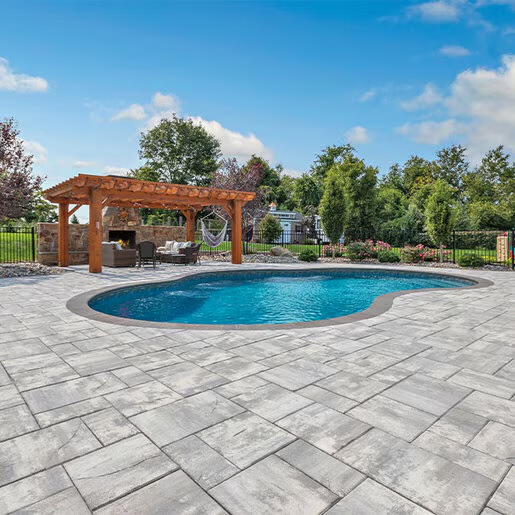 Freeform pool with stone paver patio, wood pergola, and outdoor fireplace