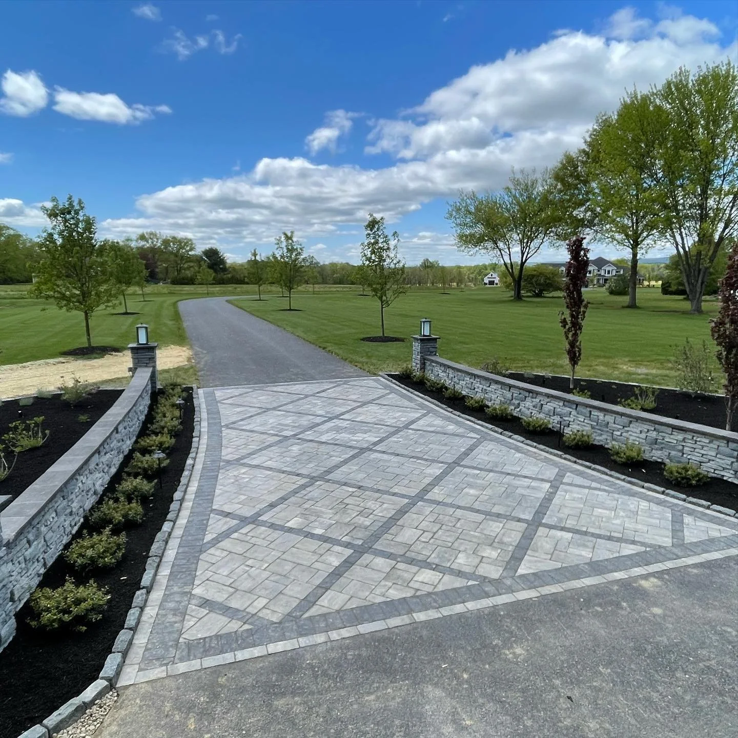 Long driveway with decorative diamond paver inlay and stone entrance walls