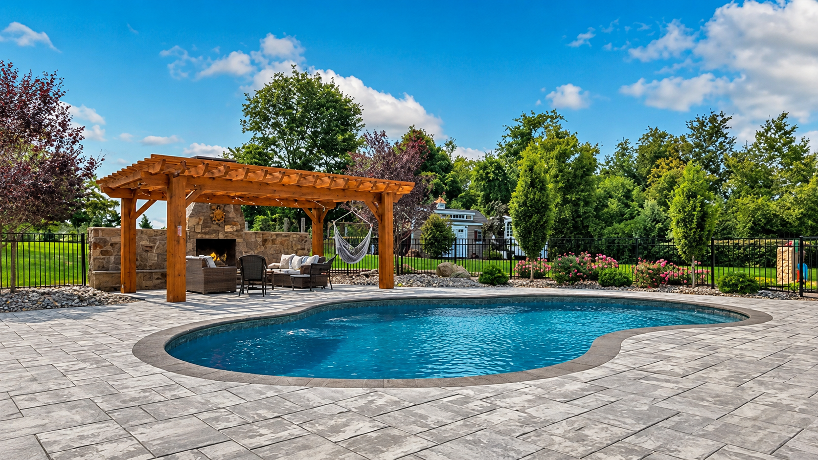 Freeform pool with stone paver patio, wood pergola, and outdoor fireplace